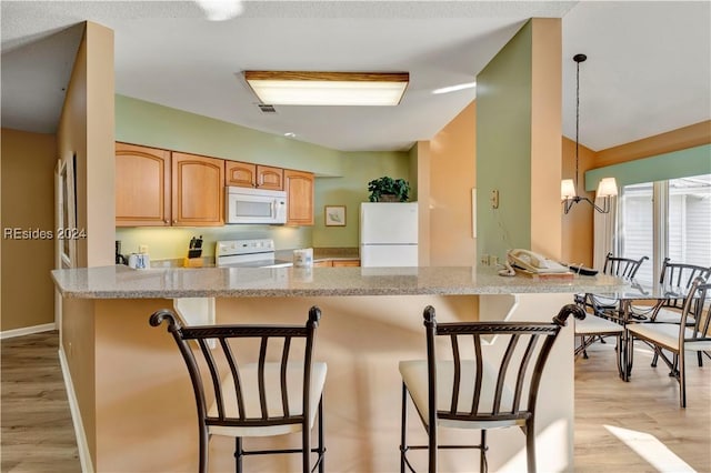 kitchen with white appliances, hanging light fixtures, a breakfast bar area, and light wood-type flooring