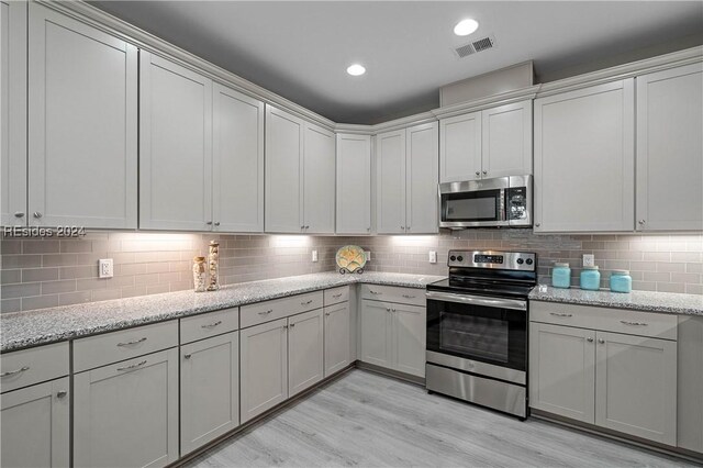 kitchen with stainless steel appliances, light stone countertops, backsplash, and light hardwood / wood-style flooring