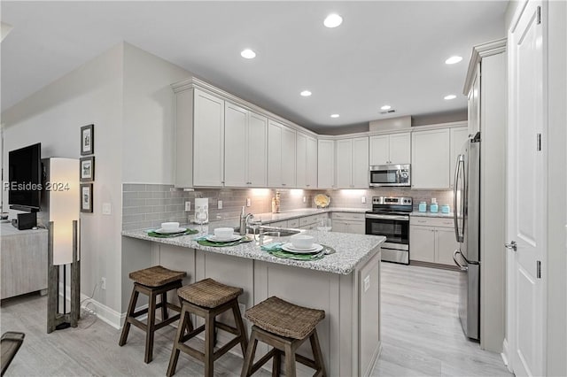 kitchen with white cabinets, a kitchen bar, light stone counters, kitchen peninsula, and stainless steel appliances