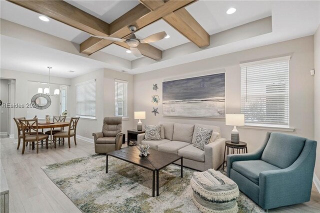 living room featuring ceiling fan with notable chandelier, light hardwood / wood-style flooring, beamed ceiling, and plenty of natural light