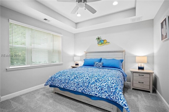 carpeted bedroom with ceiling fan and a raised ceiling