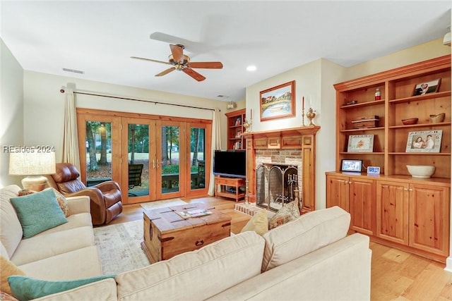 living room featuring a fireplace, ceiling fan, and light wood-type flooring