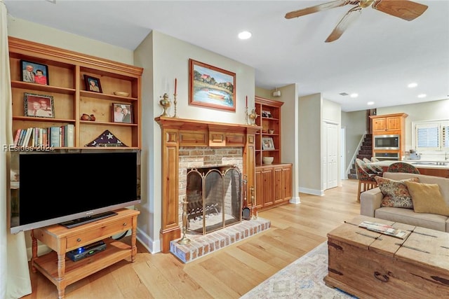 living room featuring ceiling fan, a brick fireplace, and light wood-type flooring