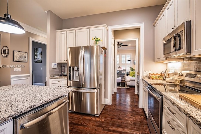 kitchen with dark wood-type flooring, appliances with stainless steel finishes, white cabinetry, hanging light fixtures, and light stone counters