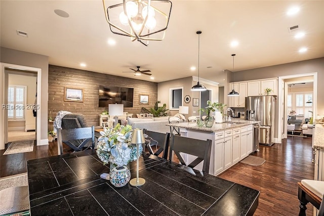 dining room with ceiling fan with notable chandelier, dark hardwood / wood-style flooring, sink, and wood walls