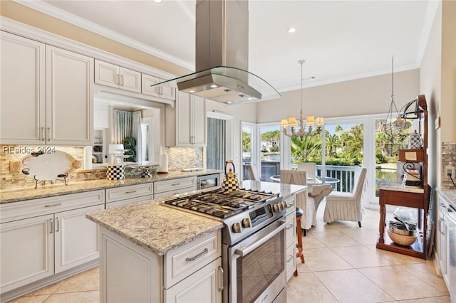 kitchen featuring stainless steel gas range, island range hood, hanging light fixtures, light stone countertops, and backsplash