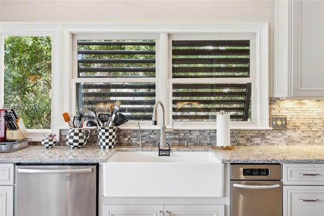 kitchen featuring white cabinetry, dishwasher, sink, backsplash, and light stone countertops