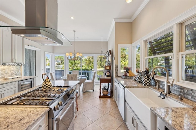 kitchen featuring pendant lighting, appliances with stainless steel finishes, light stone counters, island range hood, and beverage cooler