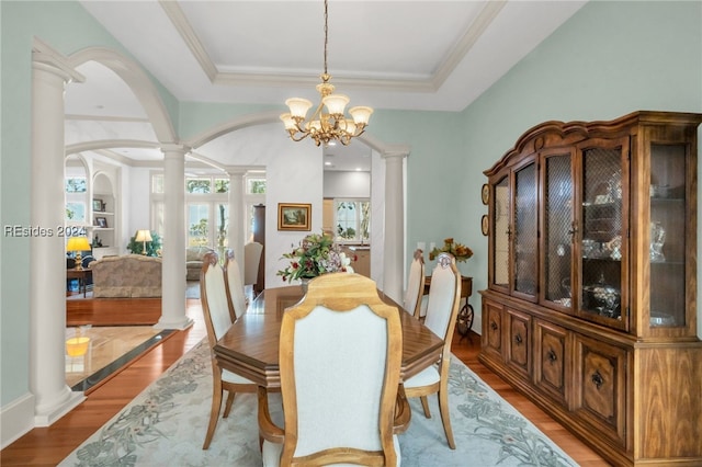 dining space with a chandelier, a raised ceiling, light wood-type flooring, and ornate columns