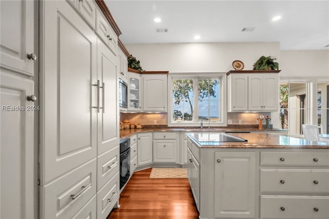 kitchen featuring black oven, backsplash, stainless steel microwave, a wealth of natural light, and white cabinets