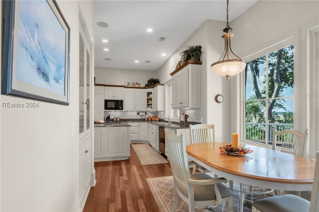 kitchen with decorative light fixtures, wood-type flooring, sink, white cabinets, and black appliances