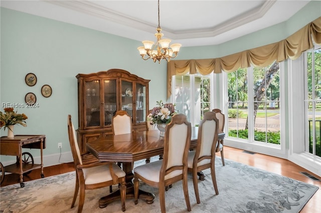 dining space with a notable chandelier, crown molding, light hardwood / wood-style flooring, and a raised ceiling