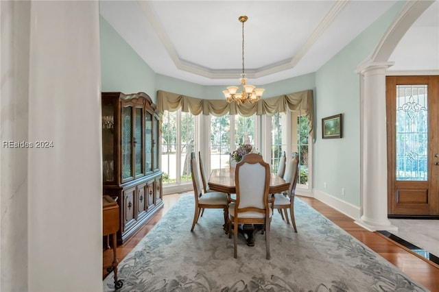 dining room with a chandelier, wood-type flooring, a raised ceiling, and ornate columns