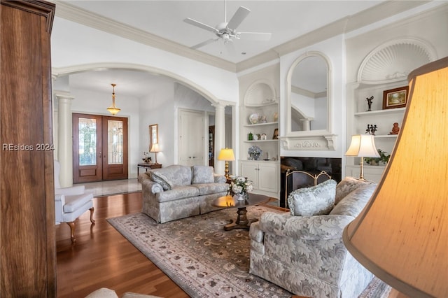 living room featuring built in shelves, french doors, ornate columns, crown molding, and hardwood / wood-style floors