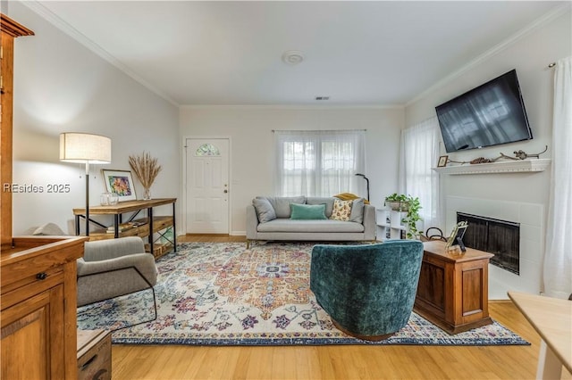 living room with crown molding, a tile fireplace, and hardwood / wood-style flooring