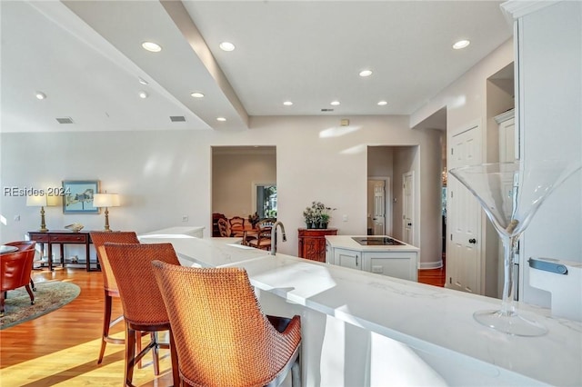 interior space with white cabinetry, black electric stovetop, light stone countertops, a kitchen island, and light wood-type flooring