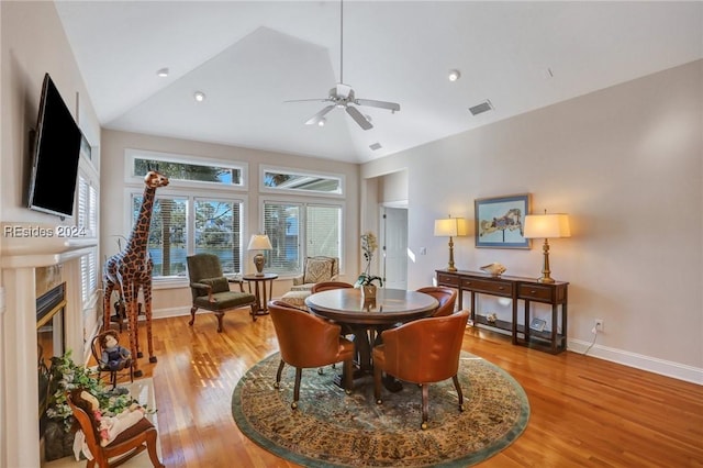 dining space featuring ceiling fan, lofted ceiling, a fireplace, and light hardwood / wood-style floors