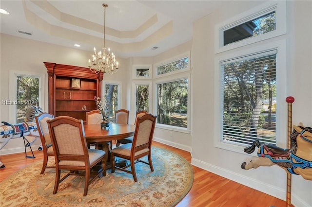 dining space with a tray ceiling, light hardwood / wood-style floors, a chandelier, and a healthy amount of sunlight