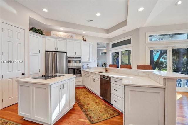 kitchen with sink, light hardwood / wood-style flooring, appliances with stainless steel finishes, white cabinets, and a kitchen island