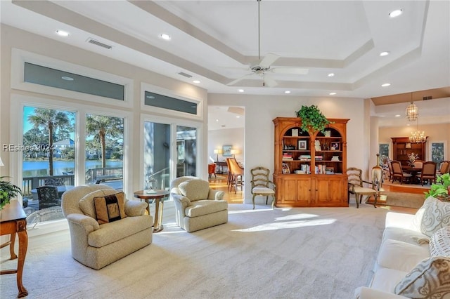 living room featuring a tray ceiling, carpet floors, a chandelier, and a water view