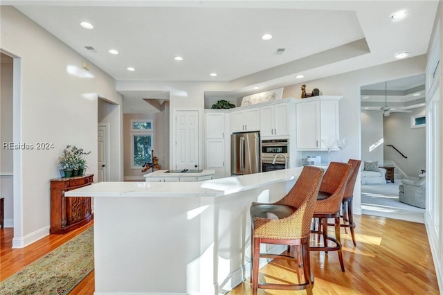 kitchen with appliances with stainless steel finishes, a breakfast bar, white cabinets, a center island, and light wood-type flooring