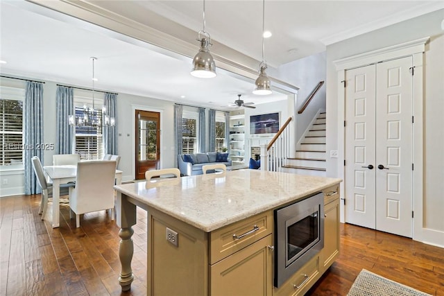 kitchen with a kitchen island, stainless steel microwave, decorative light fixtures, dark hardwood / wood-style flooring, and light stone counters