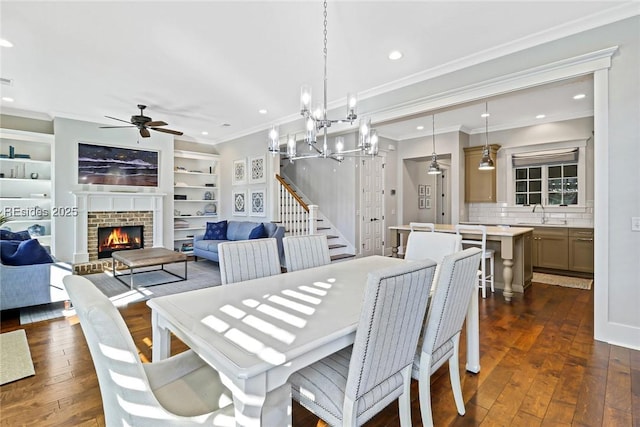 dining space featuring built in features, dark hardwood / wood-style floors, a fireplace, ornamental molding, and ceiling fan with notable chandelier