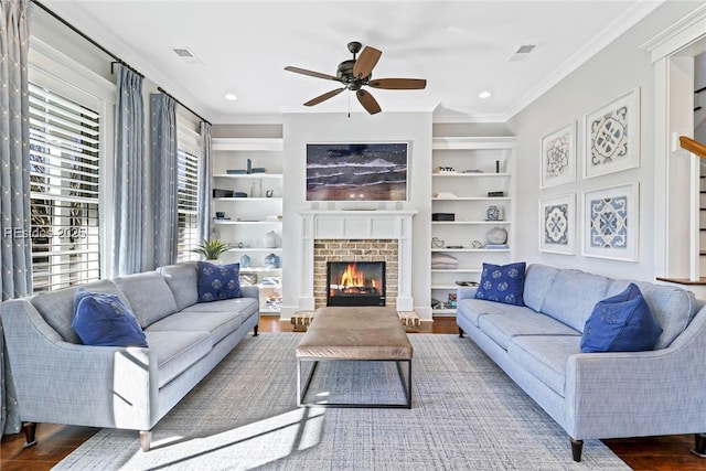 living room with ornamental molding, a brick fireplace, hardwood / wood-style floors, and built in features