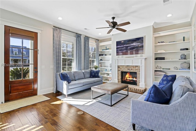 living room featuring dark hardwood / wood-style flooring, a fireplace, built in features, and ceiling fan