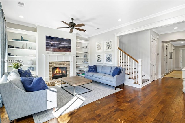 living room featuring dark hardwood / wood-style flooring, ceiling fan, crown molding, a brick fireplace, and built in shelves