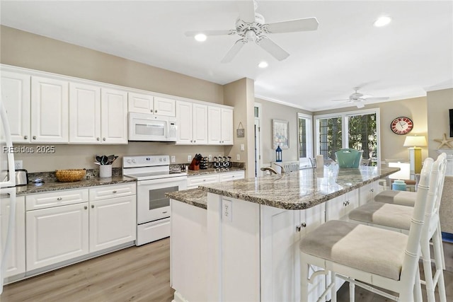 kitchen featuring white cabinetry, a breakfast bar area, dark stone counters, a kitchen island with sink, and white appliances