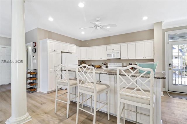 kitchen featuring white appliances, light hardwood / wood-style flooring, dark stone countertops, white cabinets, and a kitchen bar