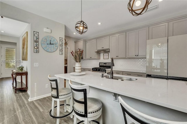 kitchen featuring a kitchen bar, gray cabinetry, hanging light fixtures, stainless steel stove, and light hardwood / wood-style floors