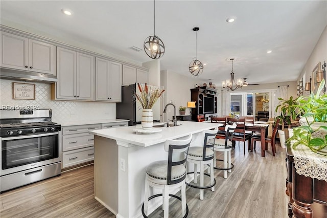 kitchen with gray cabinets, appliances with stainless steel finishes, an island with sink, hanging light fixtures, and light hardwood / wood-style floors