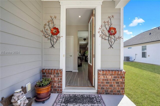 doorway to property with central AC unit and a lawn