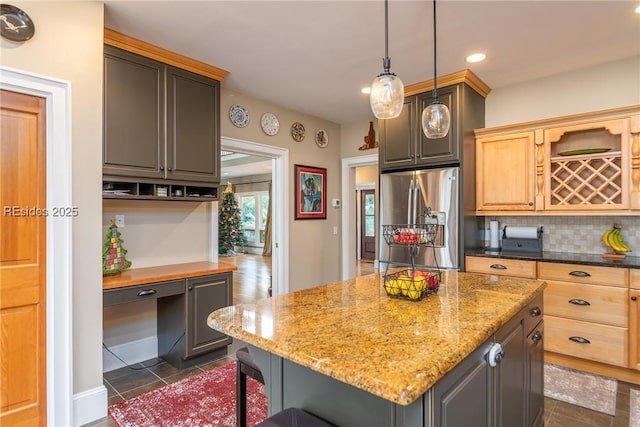 kitchen with built in desk, a kitchen island, light brown cabinetry, stainless steel fridge with ice dispenser, and dark stone counters