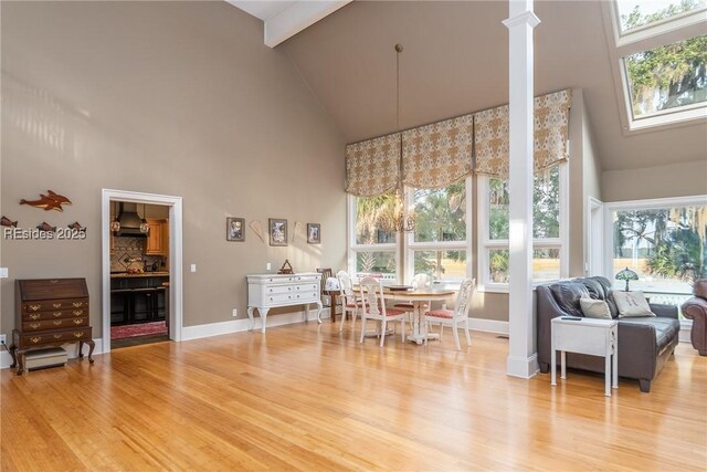 dining room featuring beam ceiling, a towering ceiling, and light hardwood / wood-style flooring