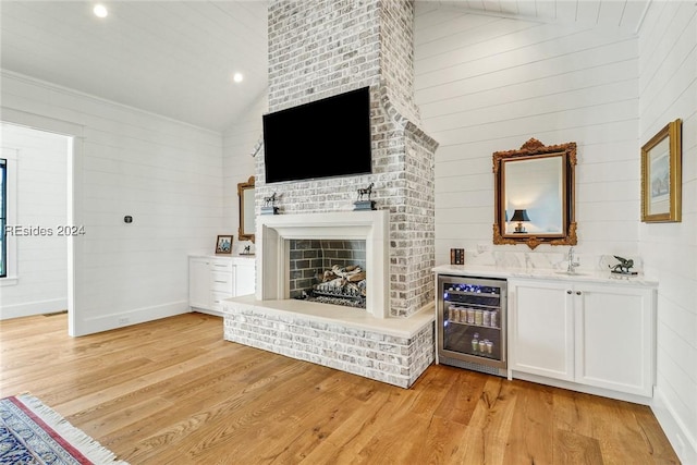 unfurnished living room featuring beverage cooler, high vaulted ceiling, a brick fireplace, and light wood-type flooring