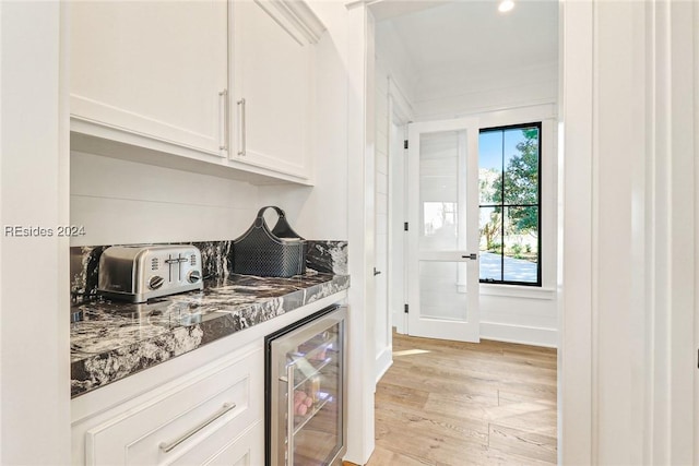 bar with wine cooler, white cabinetry, light hardwood / wood-style flooring, and dark stone counters