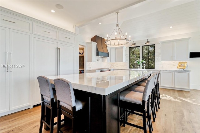 kitchen with a kitchen bar, custom exhaust hood, light stone counters, a center island, and hanging light fixtures