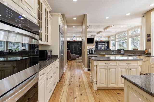 kitchen with light hardwood / wood-style flooring, beverage cooler, cream cabinetry, dark stone counters, and stainless steel double oven