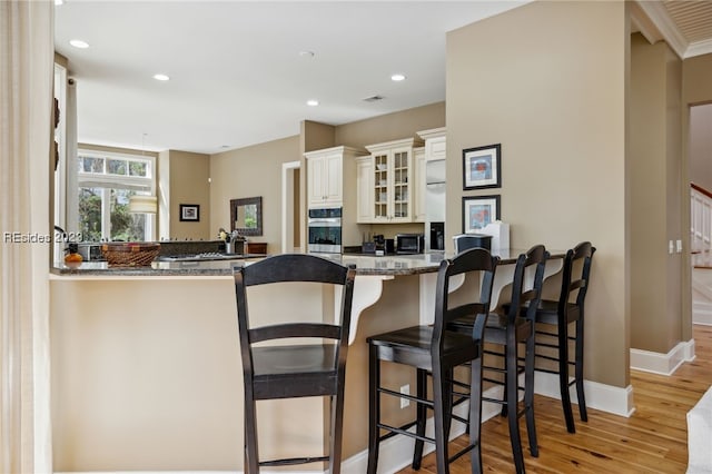 kitchen with a breakfast bar, light stone counters, kitchen peninsula, light hardwood / wood-style floors, and white cabinets