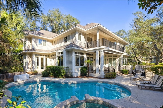 back of property featuring a balcony, a pool with hot tub, and a patio