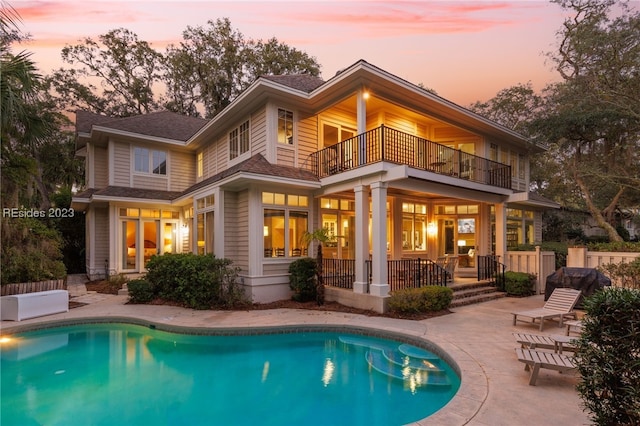 back house at dusk featuring a balcony, a fenced in pool, and a patio