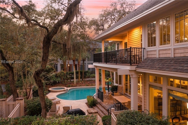 pool at dusk featuring an in ground hot tub and a patio