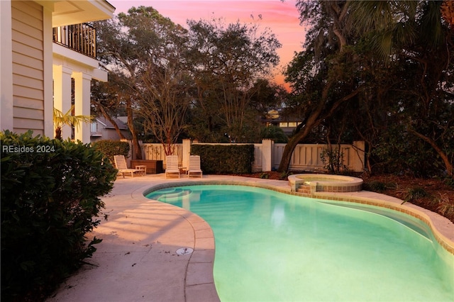 pool at dusk with an in ground hot tub and a patio area