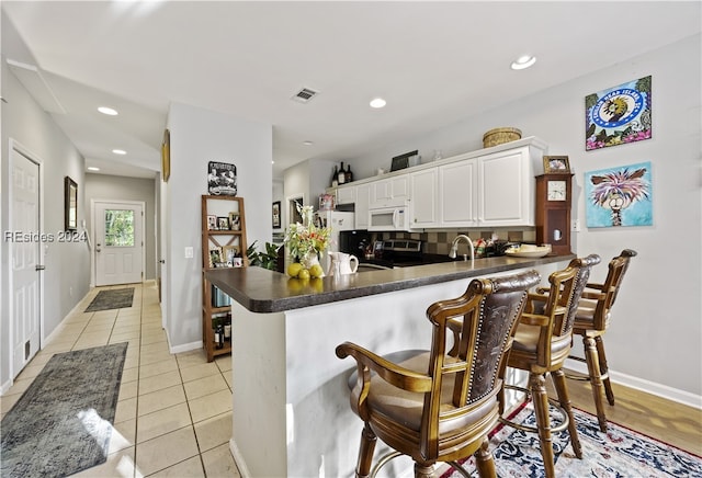 kitchen featuring light tile patterned flooring, tasteful backsplash, electric range, kitchen peninsula, and white cabinets