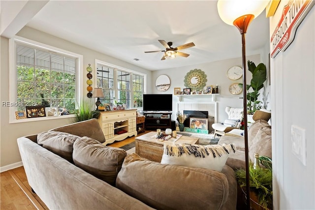 living room featuring hardwood / wood-style floors, a tile fireplace, a healthy amount of sunlight, and ceiling fan