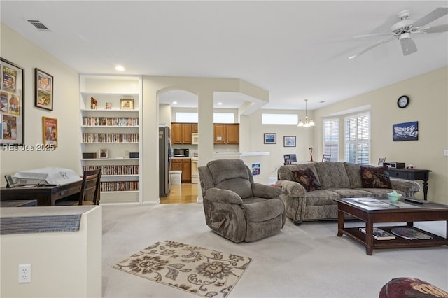 living room featuring light colored carpet, ceiling fan with notable chandelier, and built in features