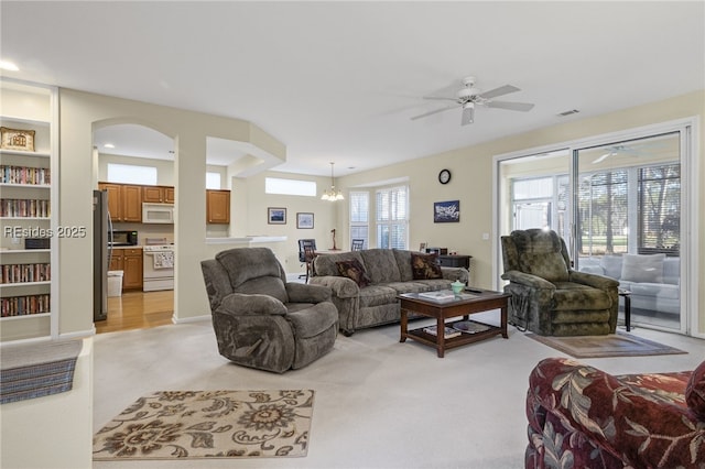 carpeted living room featuring ceiling fan with notable chandelier and built in features